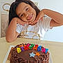 child, birthday, cake, chocolate, candles, smile, happy, long_hair, white_shirt, table, celebration, party, colorful, posing, indoor, food, dessert, cute, face, hands