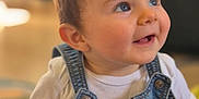 Margot a rejoint le concours — aidez-le/la à gagner de superbes lots ! baby, child, smiling, denim_overalls, white_shirt, blue_eyes, face, hair, portrait, indoor, happy, cute, infant, sitting, clothing, person, skin, young, cheerful, toddler