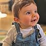 baby, child, smiling, denim_overalls, white_shirt, blue_eyes, face, hair, portrait, indoor, happy, cute, infant, sitting, clothing, person, skin, young, cheerful, toddler