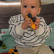 Tilio participe au concours pour gagner de l'argent avec cette photo : child, toddler, baby, face, toy_bulldozer, toy_car, striped_shirt, beige_pants, blanket, sofa, indoor, sitting, hands, play, curious, big_eyes, portrait, living_room, carpet, cute