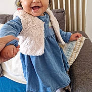 Laïa a rejoint le concours — aidez-le/la à gagner de superbes lots ! baby, child, toddler, smiling, happy, headband, bow, blue_dress, fur_vest, white_shoes, sneakers, curly_hair, holding_hand, couch, pillow, radiator, indoor, portrait, standing, playful