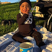 Saint joined the competition — help win amazing prizes! baby, child, snack, blanket, grass, stroller, sunlight, outdoor, blue_sky, hat, bib, shoes, can, person, sitting, smiling, face, toy, playtime, leisure