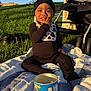 baby, child, snack, blanket, grass, stroller, sunlight, outdoor, blue_sky, hat, bib, shoes, can, person, sitting, smiling, face, toy, playtime, leisure