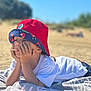 beach, blue_sky, casual_clothing, child, daylight, hat, outdoor, person, portrait, red_hat, relaxing, resting, sand, sky, summer, thinking, towel, vacation, white_shirt, young