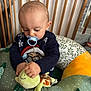 Nino a rejoint le concours — aidez-le/la à gagner de superbes lots ! baby, pacifier, plush_toy, turtle, baby_seat, crib, sweater, child, indoor, wooden_crib, toy, infant, cute, smiling_toy, child_playing, blue_pacifier, knitwear, green, yellow, red