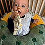 baby, child, teething_toy, giraffe_toy, cushion, crib, infant, bib, hand, face, wide_eyes, sitting, indoor, comfort, home, soft_toy, polka_dot, green, yellow, wooden