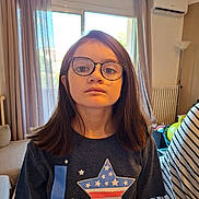 Charlène a rejoint le concours — aidez-le/la à gagner de superbes lots ! child, girl, glasses, indoor, shirt, star_pattern, curtains, window, radiator, toy, home, casual_clothing, brown_hair, portrait, young, person, furniture, light, expressionless, background
