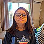 child, girl, glasses, indoor, shirt, star_pattern, curtains, window, radiator, toy, home, casual_clothing, brown_hair, portrait, young, person, furniture, light, expressionless, background