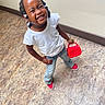 child, girl, smiling, standing, white_shirt, denim_jeans, red_shoes, braided_hair, beads, purse, red_purse, floor_tiles, indoor, happy, cute, fashion, playful, person, casual, portrait