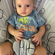 Xander is registered to the contest to win money with this photo: baby, child, infant, blue_shirt, text, mr_cool, cushion, pattern, plush_toy, hand, legs, sitting, indoors, cute, person, portrait, young_child, expression, clothing, soft_toy