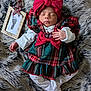 baby, newborn, sleeping, plaid_dress, red_bow, headband, white_clothing, fur_blanket, footprint_frame, wooden_frame, hand, infant, cozy, holiday, portrait, soft_texture, cute, peaceful, indoors, lying_down