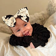 Lydia is registered to the contest to win money with this photo: baby, bow, black_clothing, blanket, closeup, cute, face, happy, headwear, infant, lying_down, person, portrait, resting, smiling, soft_texture, tongue_out, white_blanket, young_child, indoors