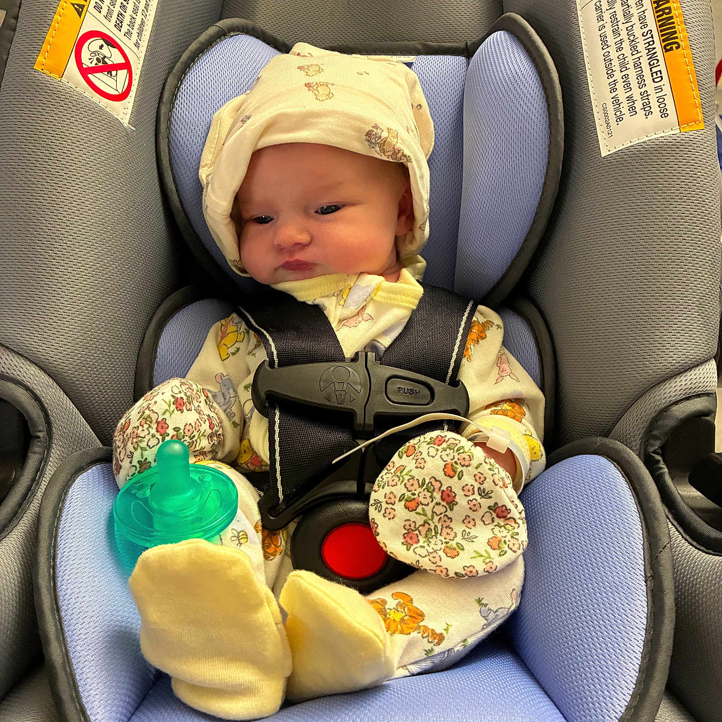 Roselynn is registered to the contest to win money with this photo: baby, infant, car_seat, buckled, harness, pacifier, yellow_clothing, floral_pattern, bonnet, socks, seated, portrait, face, eyes, indoors, vehicle, safety, baby_gear, closeup, photography