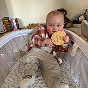 Malo participe au concours pour gagner de l'argent avec cette photo : baby, child, playpen, plaid_shirt, beige_pants, socks, wooden_disc, chewing, indoor, living_room, books, teddy_bear, clock, smiling, cute, infant, person, home, cozy, portrait