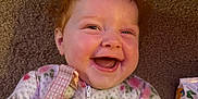 Iris joined the competition — help win amazing prizes! baby, smiling, red_hair, curly_hair, floral_clothing, onesie, carpet, happy, infant, cute, child, portrait, lying_down, indoors, cozy, cheerful, young_child, face, skin, hand