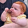 Iris is registered to the contest to win money with this photo: baby, child, red_hair, eating, meat, hand, face, person, arm, yellow_clothing, outdoor, fence, adult, holding, closeup, skin, cheek, casual, summer, happy