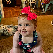 Iris is registered to the contest to win money with this photo: baby, child, smile, bow, headband, carpet, indoor, kitchen, chair, table, floor, person, red_hair, clothing, seat, furniture, dining_room, happy, toddler, cute