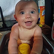 Memphis is registered to the contest to win money with this photo: baby, infant, sink, water, bath, smiling, happy, blue_eyes, wet_skin, toy, yellow, household, cleaning_product, kitchen, child, person, cute, playful, indoor, portrait