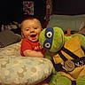 baby, child, smiling, happy, plush_toy, teenage_mutant_ninja_turtle, pillow, bedroom, indoor, cuddling, red_shirt, foot, cozy, furniture, soft_toy, portrait, infant, cute, toy, home