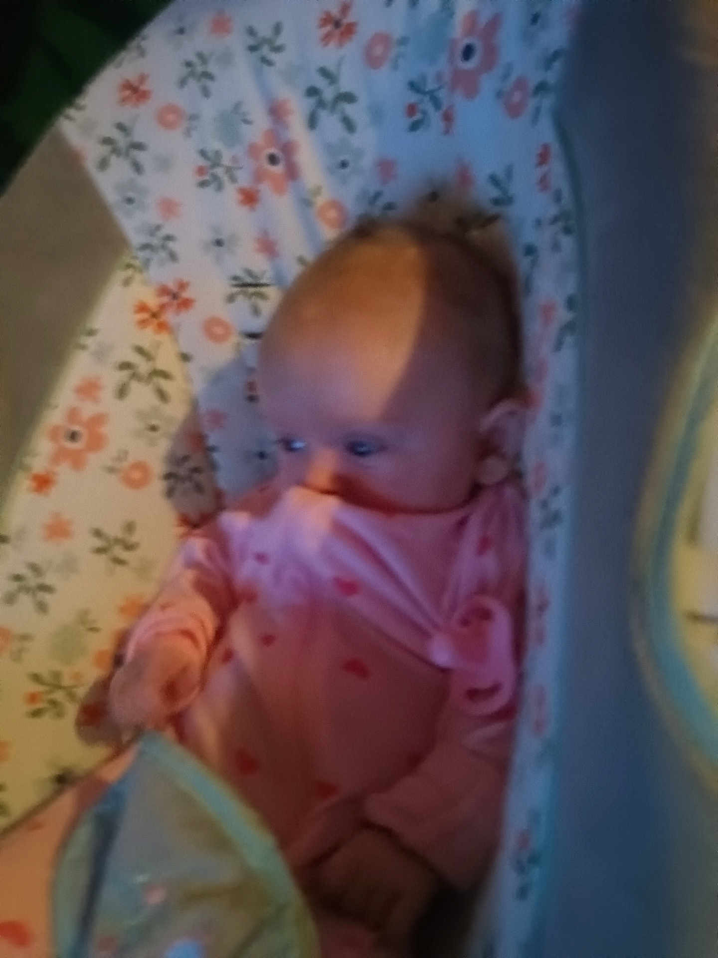 Emma joined the competition — help win amazing prizes! baby, infant, newborn, bassinet, crib, bedding, floral_pattern, onesie, pink_clothing, face, head, hand, blanket, mattress, indoors, portrait, blurry, low_light, shadow, sleepy