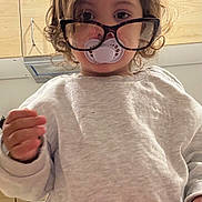 Charli a rejoint le concours — aidez-le/la à gagner de superbes lots ! appliance, baby, cabinet, casual_clothing, child, curious, curly_hair, cute, face, glasses, hand, indoor, kitchen, pacifier, person, portrait, standing, sweater, toddler, young_child
