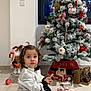 black_skirt, child, christmas_tree, curly_hair, decorations, festive, floor, holiday, indoor, ornaments, pine_cones, pink_shoes, playful, sitting, tea_set, toddler, toy, toy_stroller, white_shirt, window