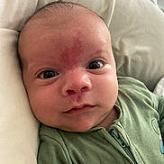 Elliot is registered to the contest to win money with this photo: baby, infant, face, eyes, green_onesie, skin, newborn, portrait, closeup, expression, human, child, soft_surface, lying_down, red_mark, cute, small, person, indoors, baby_clothing