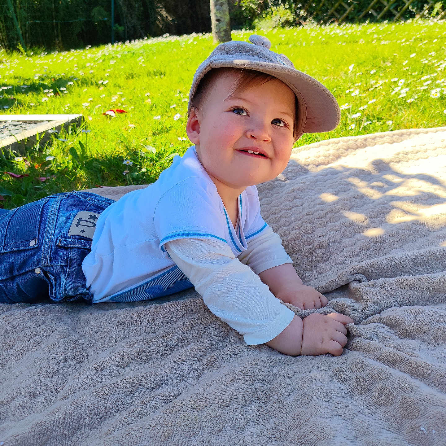 Valentin a rejoint le concours — aidez-le/la à gagner de superbes lots ! baby, blanket, cap, casual_clothing, child, face, flower, grass, greenery, happy, jeans, nature, outdoor, playful, portrait, smile, summer, sunlight, toddler, white_shirt