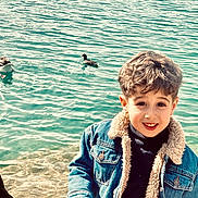 élan participe au concours pour gagner de l'argent avec cette photo : child, boy, smile, curly_hair, denim_jacket, water, lake, ducks, outdoor, nature, casual_clothing, happy, portrait, young, people, animal, bird, sunlight, face, shore