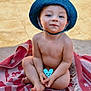 baby, bodypart, bonnet, cap, clothing, dress, face, finger, hand, happy, hat, head, person, photography, portrait, sitting, smile, sunhat, swimwear, towel