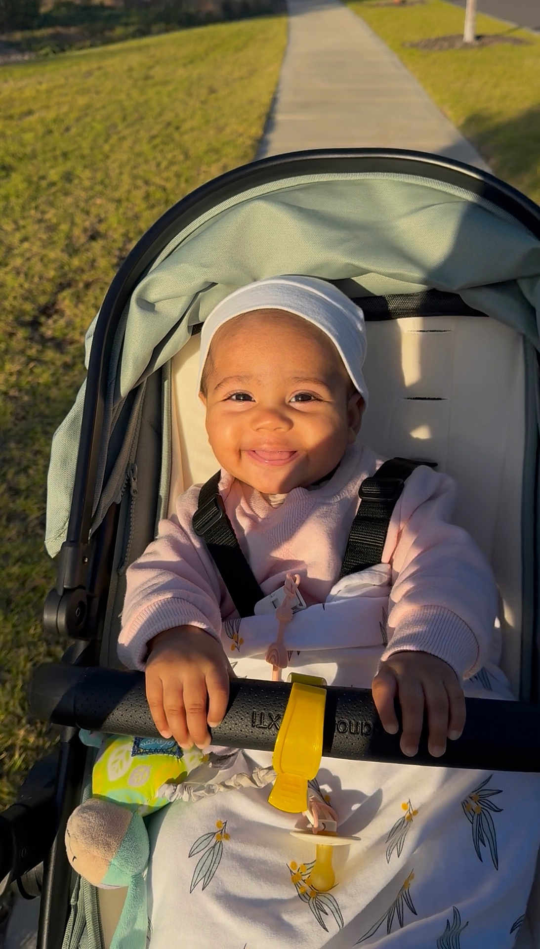 Aurohmie is registered to the contest to win money with this photo: baby, blanket, child, daytime, face, grass, hands, happy, hat, infant, outdoor, pacifier, park, pathway, seatbelt, smiling, stroller, sunlight, sweater, toy