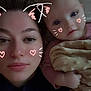 woman, baby, face, portrait, selfie, lying_down, blanket, pink_clothing, digital_filter, cat_ears, heart_doodles, skin, eyes, head, hand, closeup, indoor, cute, family, together