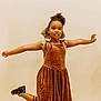 child, girl, brown_dress, velvet, black_shoes, curly_hair, pose, playful, smile, studio, beige_background, portrait, fashion, happy, full_body, studio_lighting, young, standing, arms_outstretched, kicking