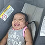 baby, car_seat, child, chubby_cheeks, clothing, cute, face, happy, head, indoor, infant, infant_girl, pink_trim, portrait, safety_label, seat, sitting, smiling, text_on_clothing, young_child