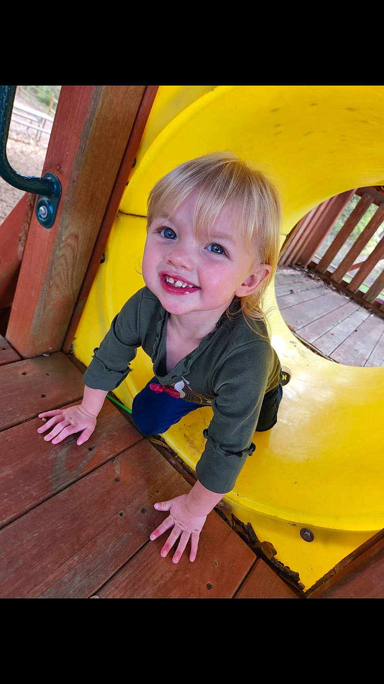 Brynnlee is registered to the contest to win money with this photo: child, toddler, playground, yellow_tunnel, wooden_deck, smiling, blonde_hair, blue_eyes, casual_clothing, outdoor, play, happy, cute, young_child, candid, daylight, fun, hands, face, person
