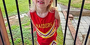 Brynnlee joined the competition — help win amazing prizes! child, cheerleader, red_dress, smiling, outdoor, deck, grass, trees, happy, young_child, blond_hair, sneakers, white_socks, raiders, sportswear, person, portrait, daylight, wooden_floor, fence