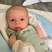 Zachary joined the competition — help win amazing prizes! baby, infant, onesie, mittens, cushion, face, eyes, floor, wooden_chair, rocking_chair, blanket, clothing, person, portrait, indoor, baby_bed, newborn, soft_toy, baby_garment, baby_accessory