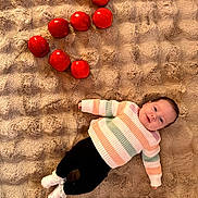 élya participe au concours pour gagner de l'argent avec cette photo : baby, black_pants, casual_clothing, child, cozy, cute, fluffy_blanket, happy, indoor, infant, lying_down, person, red_apples, relaxed, smiling, soft_texture, still_life, striped_sweater, warm_colors, white_socks