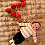 baby, black_pants, casual_clothing, child, cozy, cute, fluffy_blanket, happy, indoor, infant, lying_down, person, red_apples, relaxed, smiling, soft_texture, still_life, striped_sweater, warm_colors, white_socks