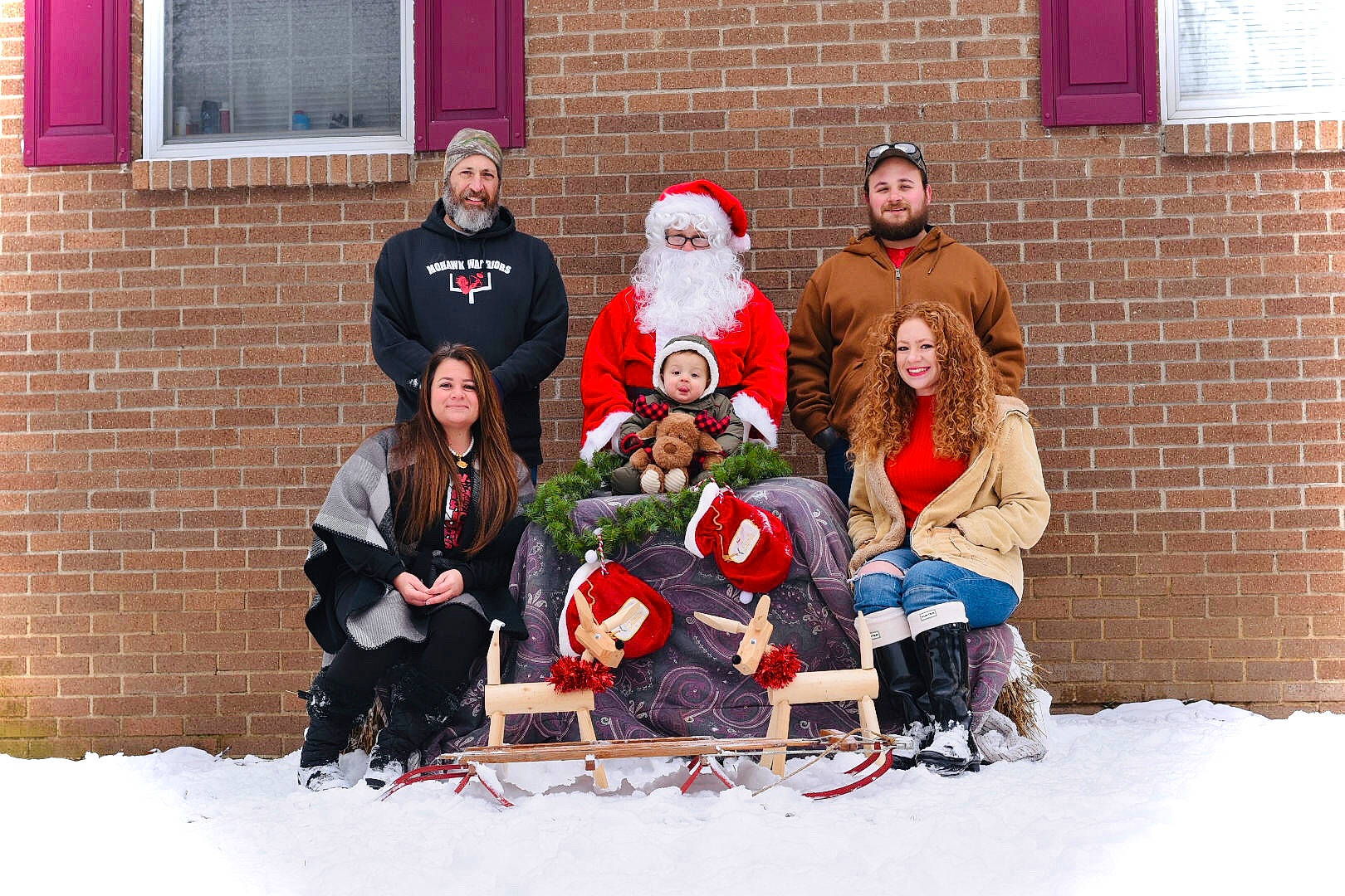 Beau is registered to the contest to win money with this photo: beard, brick, brickwork, event, freezing, fun, hat, headwear, jacket, jeans, joy, mammal, person, red, santa_claus, smile, snow, social_group, tree, trousers