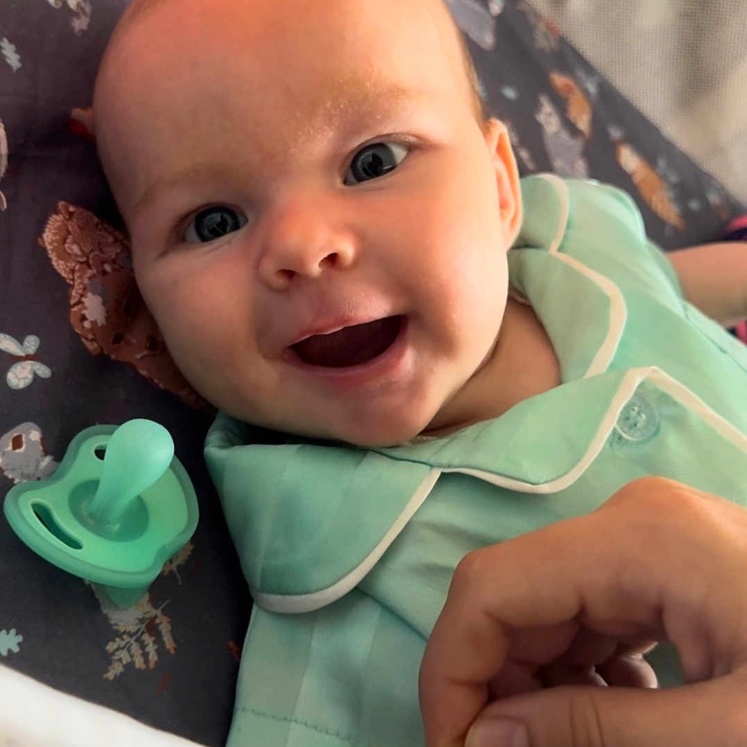 Marlowe is registered to the contest to win money with this photo: baby, babylaughing, bed, bodypart, clothing, crib, dress, face, finger, furniture, hand, happy, head, infantbed, newborn, person, photography, portrait, smile, toy