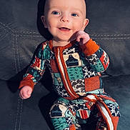 Roczen is registered to the contest to win money with this photo: baby, child, smiling, onesie, colorful_clothing, couch, indoor, footwear_free, sitting, happy, face, infant, cute, patterned_clothing, human, portrait, young_child, closeup, blue_eyes, zipped_clothing