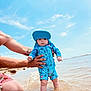 baby, child, beach, water, sun_hat, swimsuit, tattoo, person, sky, sand, ocean, summer, outdoor, holding, shore, waves, blue, cute, infant, holiday