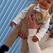 Kayden participe au concours pour gagner de l'argent avec cette photo : child, toddler, smiling, face, person, adult_hand, holding, beige_overall, white_shirt, bow_tie, black_shoes, striped_background, pampas_grass, flowers, portrait, studio_backdrop, happy, formal_clothing, celebration, hands