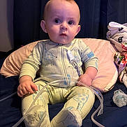 Anthony joined the competition — help win amazing prizes! baby, child, onesie, giraffe_pattern, medical_tube, pacifier, pillow, blanket, indoor, curious, sitting, soft_lighting, person, face, hand, footwear, fabric, bed, nursery, infant