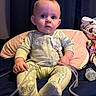 baby, child, onesie, giraffe_pattern, medical_tube, pacifier, pillow, blanket, indoor, curious, sitting, soft_lighting, person, face, hand, footwear, fabric, bed, nursery, infant