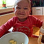 toddler, child, smiling, indoor, table, bowl, banana, food, sippy_cup, window, plant, fish_tank, photo_frame, red_shirt, wooden_table, happy, face, cute, home, natural_light