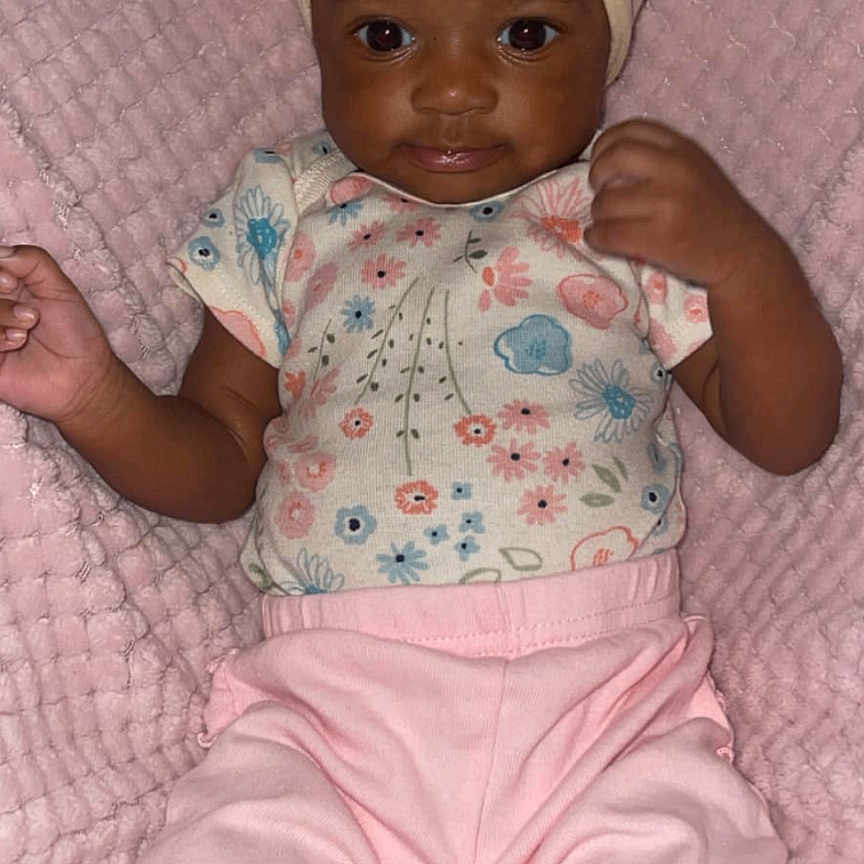Kamari is registered to the contest to win money with this photo: accessories, baby, clothing, couch, cushion, doll, dress, face, formalwear, furniture, head, headband, homedecor, linen, pants, person, photography, portrait, tie, toy