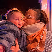 Ambre participe au concours pour gagner de l'argent avec cette photo : baby, woman, kiss, scarf, glasses, jacket, night, outdoor, happy, smile, face, hand, warm_clothing, person, portrait, love, family, affection, cheek, cozy