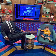 Priyansh is registered to the contest to win money with this photo: man, toddler, child, studio, television, chair, carpet, bookshelf, book, suit, tie, yellow_shirt, denim_shorts, modern, decor, smile, indoors, table, show, colorful